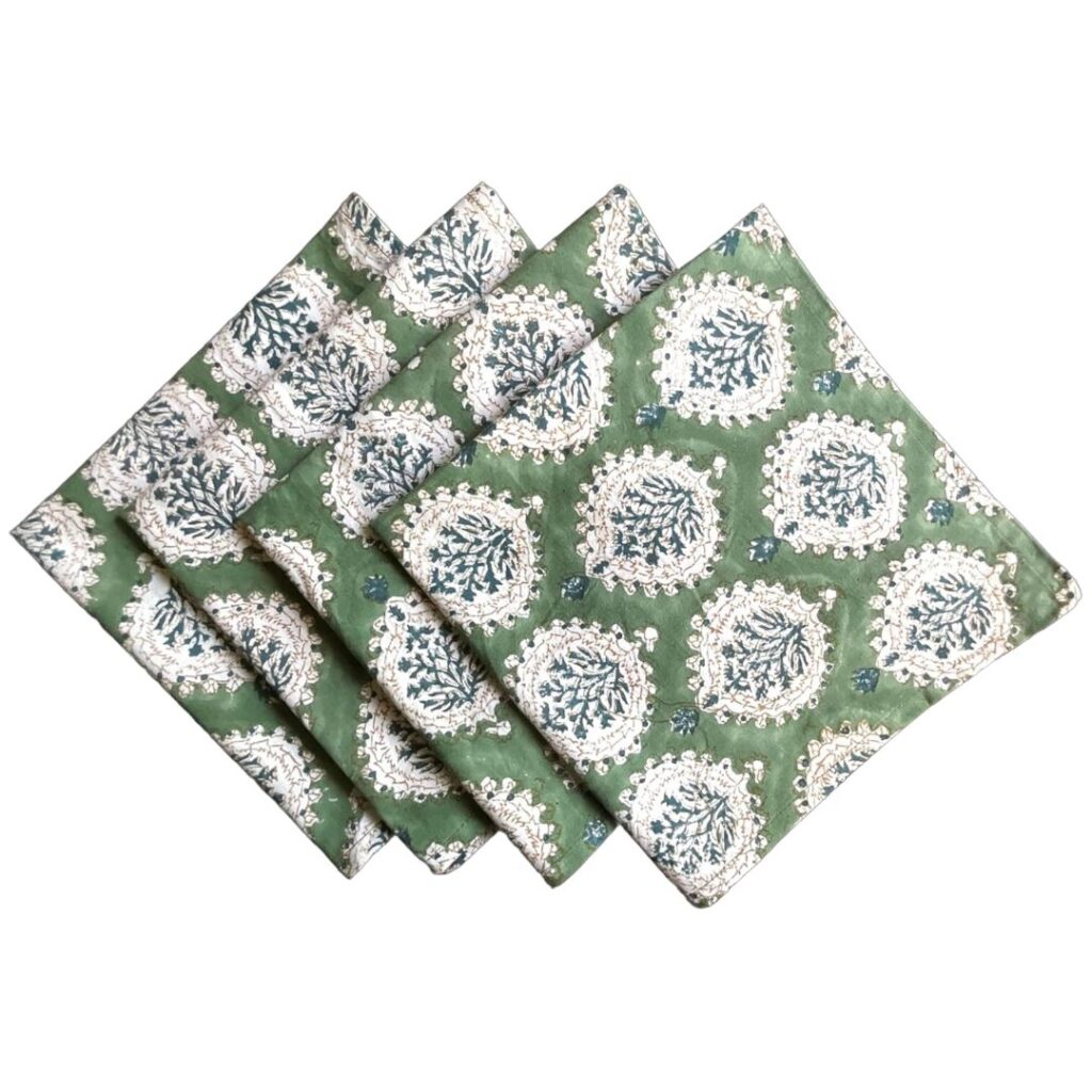 Four green fabric napkins with a white and blue circular floral pattern are neatly folded and overlapping each other, creating an elegant contrast to your DIY leather fall table decor against a plain background.