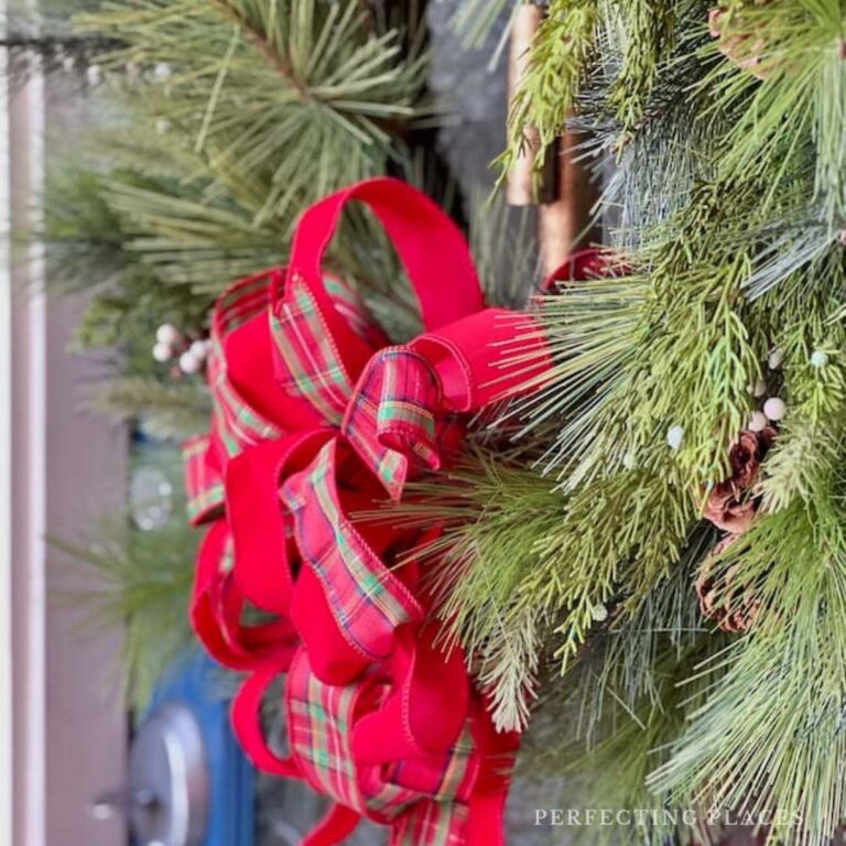 A close-up of a holiday wreath with lush green pine branches and a vibrant red plaid ribbon bow. Hung on the door, it adds a festive touch to the entrance—perfect for welcoming guests on Seven on Sunday, 11/10/24.