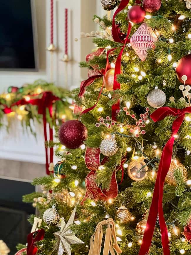 A beautifully decorated Christmas tree with red and gold ornaments, ribbons, and twinkling lights. In the background, there are festive candles and garlands on a mantel.