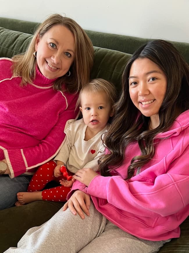 Three people sitting on a green sofa: a woman in a pink sweater, a toddler in a white shirt with red hearts, and a woman in a pink hoodie. They are smiling and relaxed—definitely one of the things I'm loving this week.