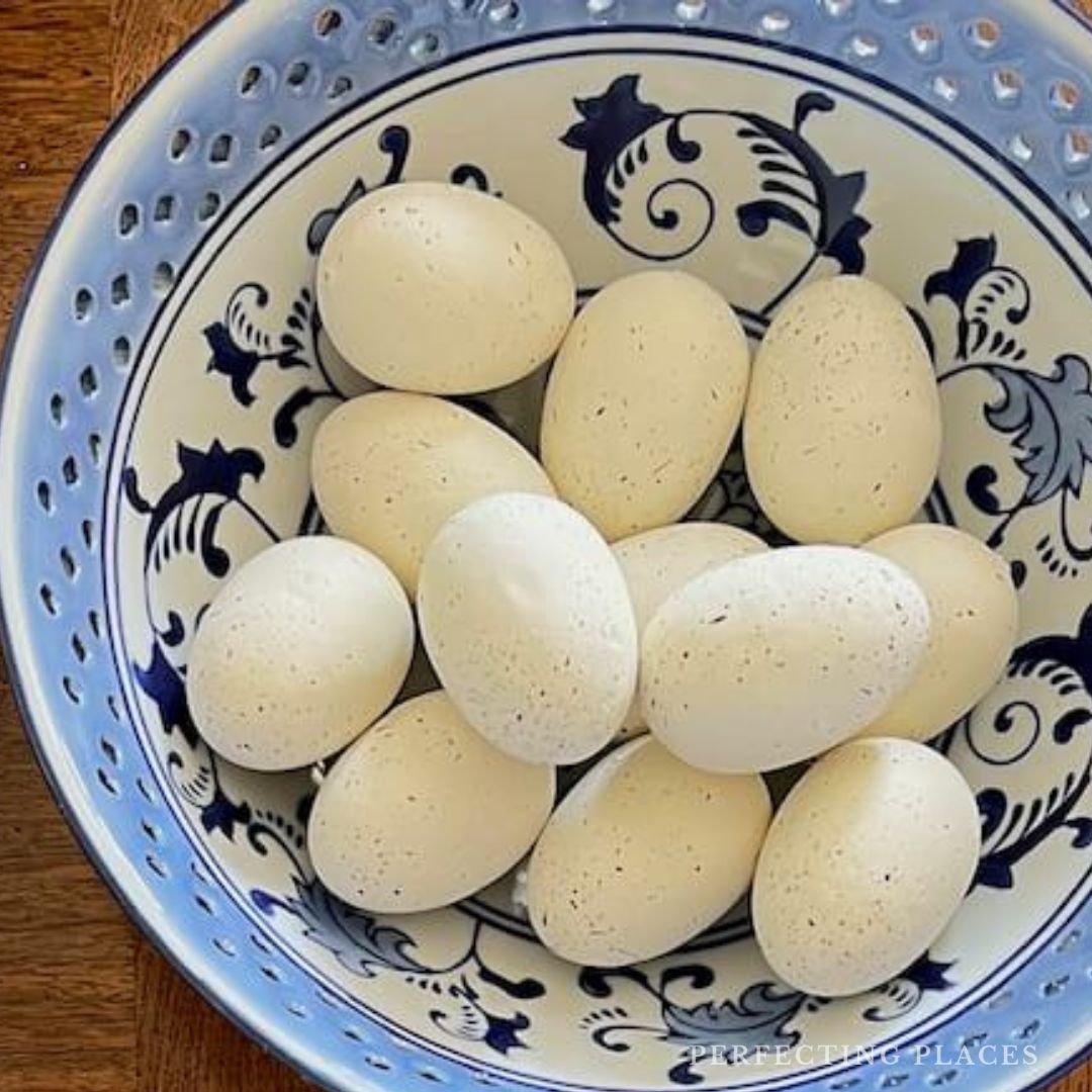 A ceramic bowl with a blue floral design holds a collection of light-colored eggs, embodying the essence of Spring Refresh. The bowl, a piece of Home Inspiration, rests gracefully on a wooden surface.