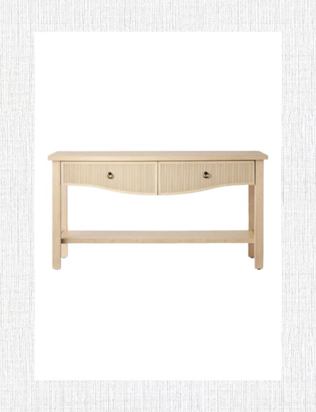 A beige wooden console table with two drawers featuring circular handles, perfect for trendy home styling. Its simple design includes a flat top, sturdy legs, and a connecting bar at the base. Ideal for spring entryway decor, it's set against a white background with a light-textured frame.