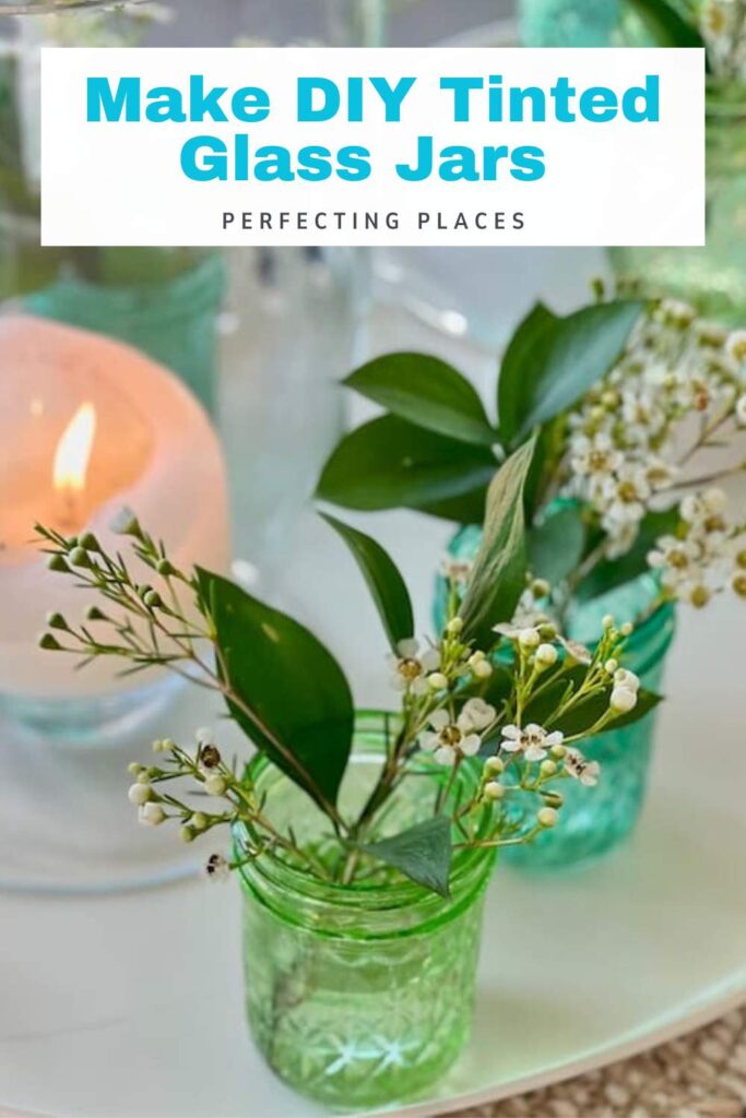 Green tinted glass jars with white flowers and green leaves, a lit candle, and the text "Make DIY Tinted Glass Jars Perfecting Places" displayed above.