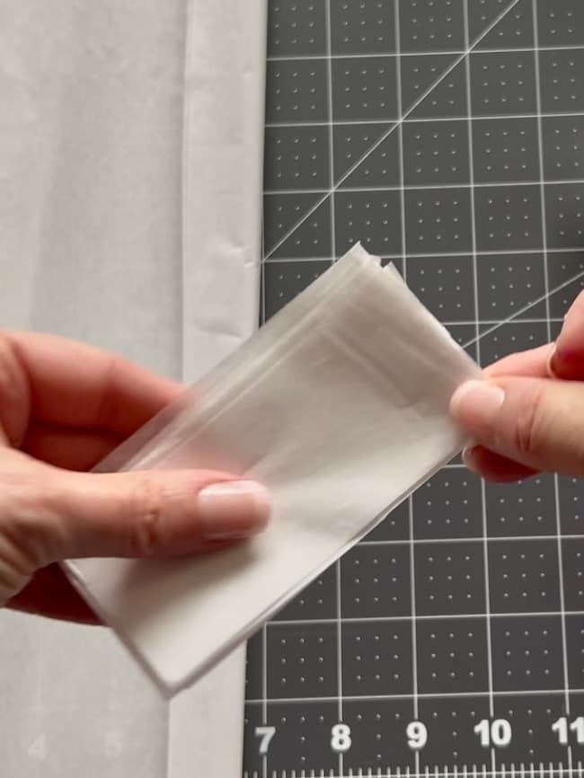 Hands gently holding folded white tissue paper against a black cutting mat with grid lines, reminiscent of delicate flowering branches in a meticulously crafted design.