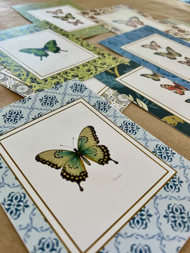 Close-up of several free printable art cards displaying butterfly illustrations, each surrounded by decorative borders in various colors and patterns. The butterflies are diverse in color and design, with the closest one showing a green and yellow butterfly.