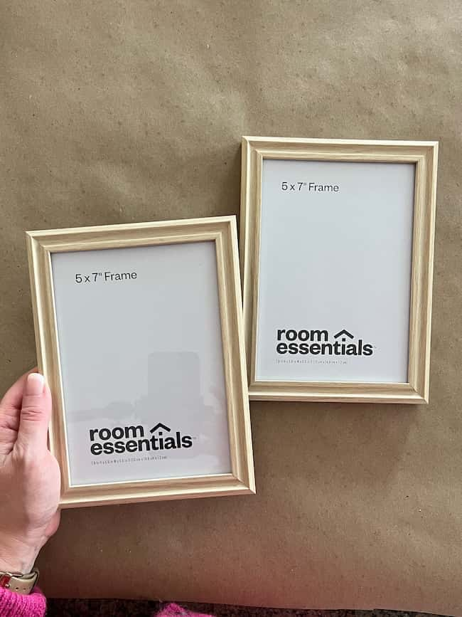 A person holding one of two wooden 5x7 inch picture frames on a brown surface, perfect for showcasing your favorite photos or free printable art. Both frames feature blank inserts labeled "room essentials.