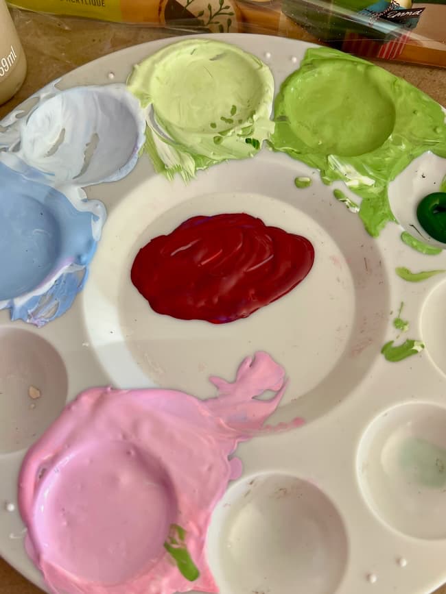 A paint palette with splashes of vibrant colors, including red, green, blue, light green, and pink. The central section boasts a large dollop of red paint—perfect for crafting hand-painted Easter eggs and adding flair to your spring decor.