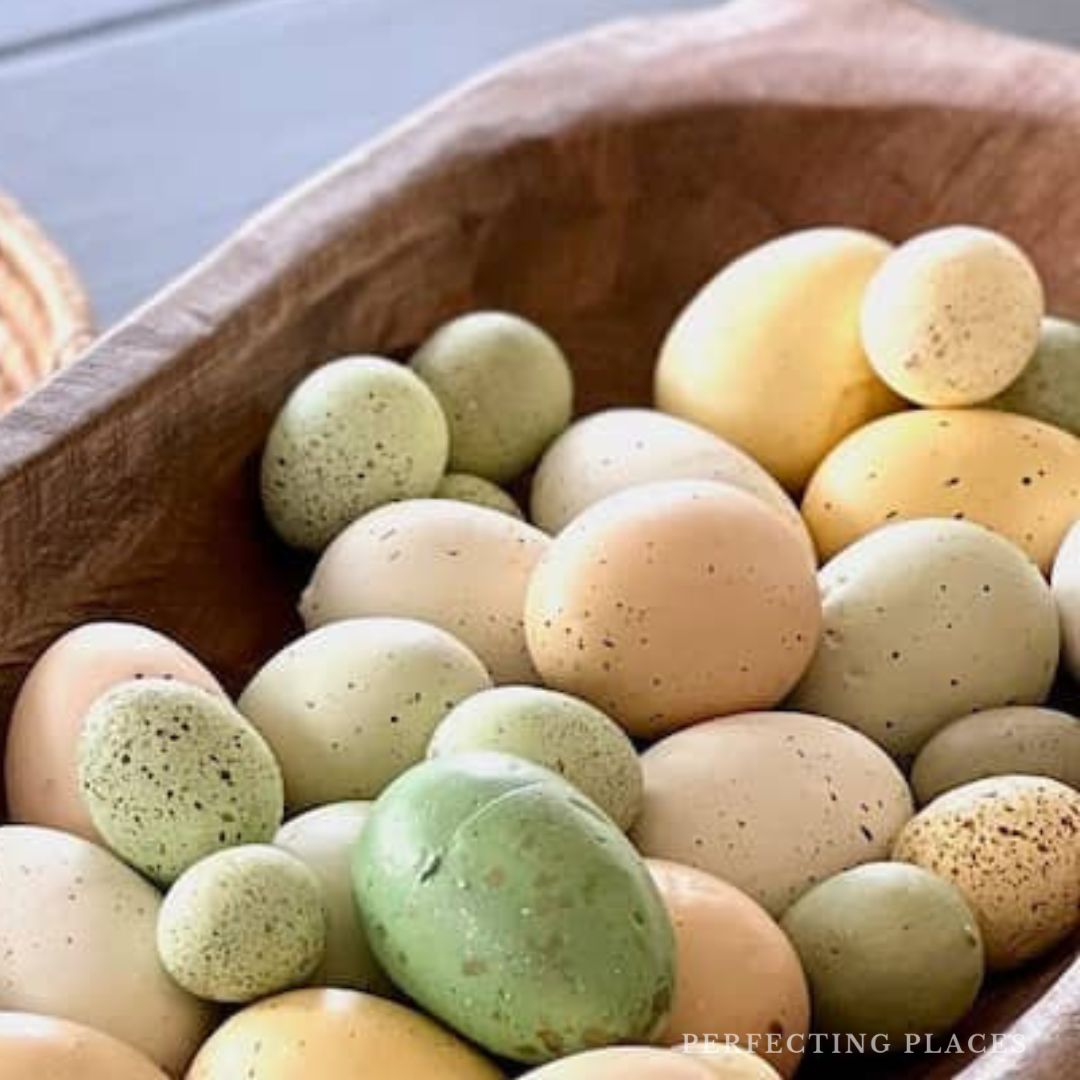 A wooden bowl filled with pastel-colored decorative eggs, featuring shades of green, yellow, and beige speckled patterns, serves as the perfect weekend find for your tabletop inspiration.