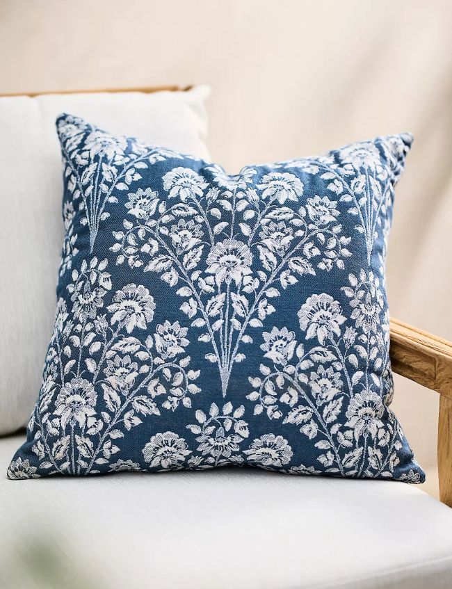 A decorative blue cushion with a white floral pattern rests on a light-colored cushioned wooden chair—one of our Top Picks for the Labor Day Sale.