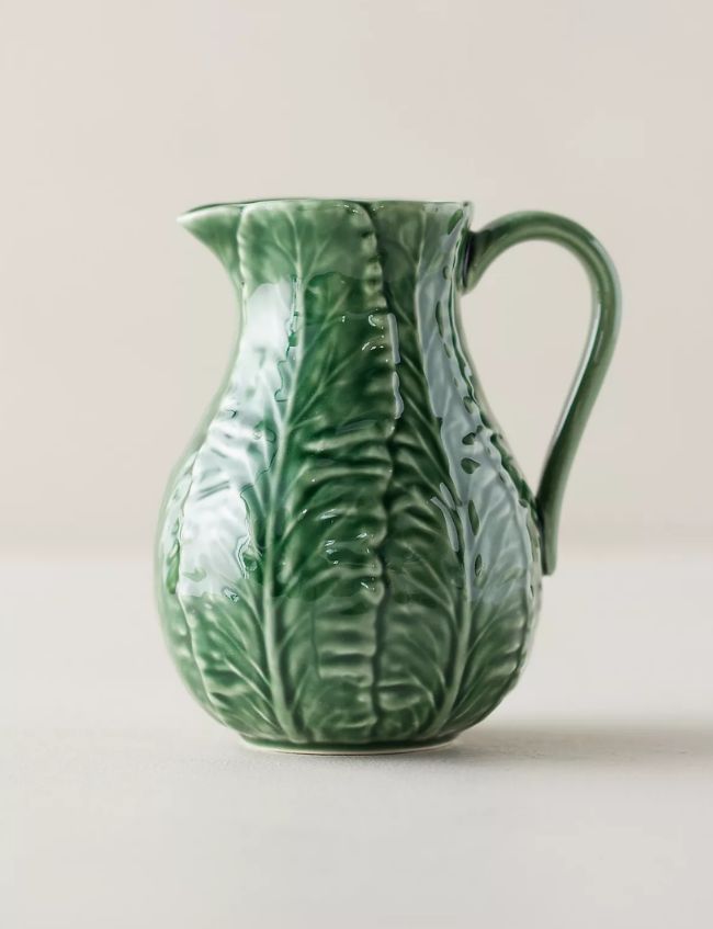 A green ceramic pitcher shaped and textured like overlapping cabbage leaves, with a curved handle and glossy finish, featured as one of our Best Picks for the Terrain Sale. Set against a neutral background.
