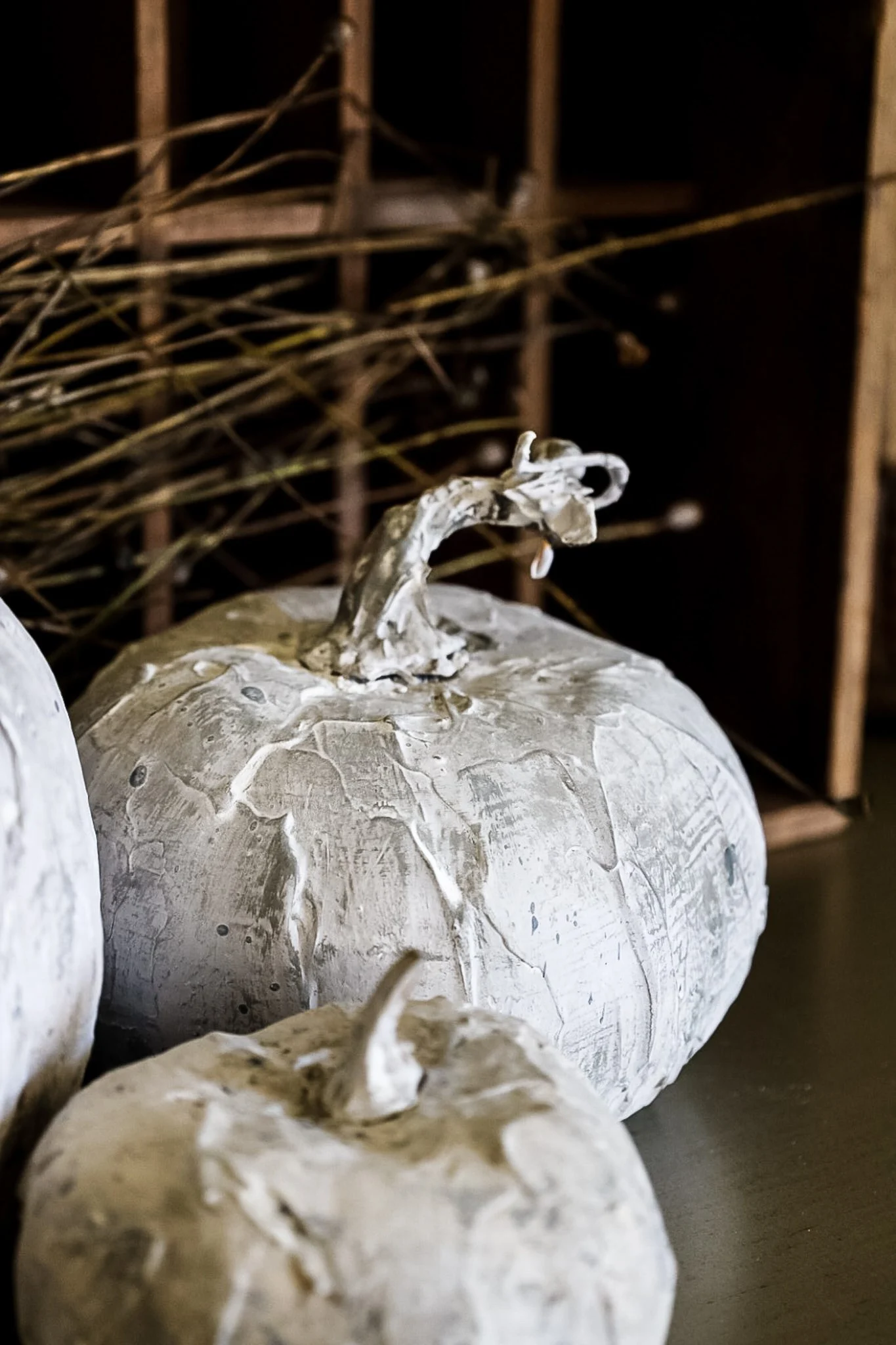 Close-up of two white, textured pumpkins with rough surfaces and twisted stems, set against a rustic background with a bundle of twigs and a wooden crate—perfect Saturday inspiration for a warm weekend.