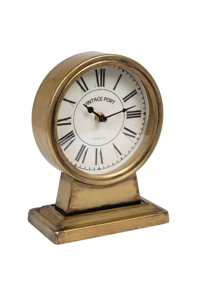 A vintage-style tabletop clock with a brass finish and Roman numerals on a white face brings timeless living room charm, pairing perfectly with green and beige accents or placed atop a rug. The rectangular base matches the elegant brass body.