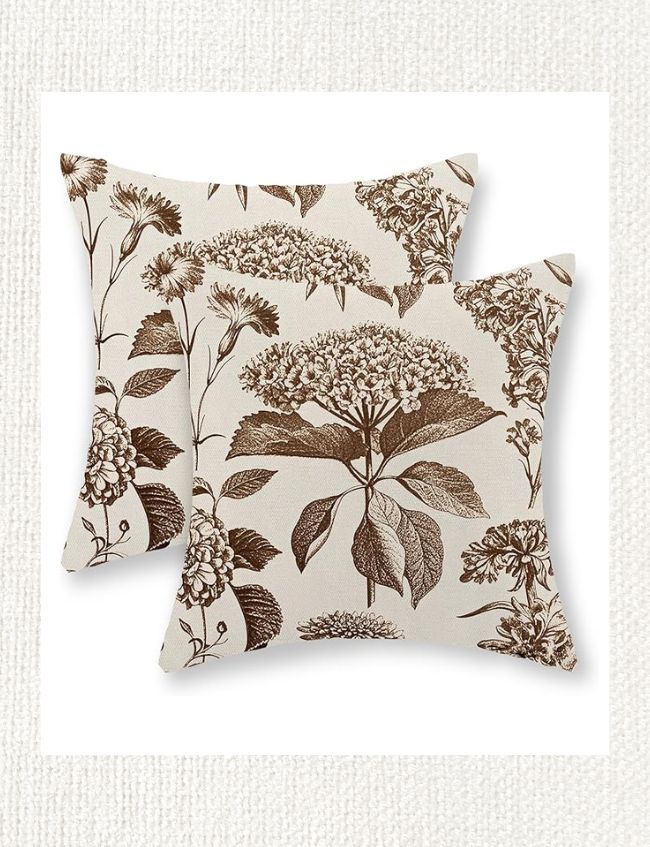 Two square decorative pillows with beige fabric and brown botanical flower and leaf prints, placed overlapping on a light textured background—perfect for adding a warm & cozy touch to your weekend inspiration.