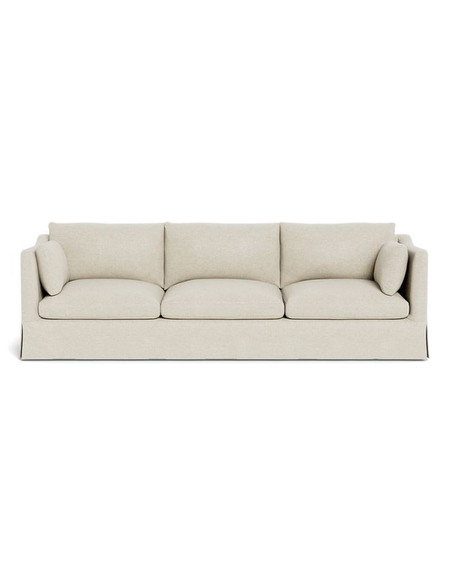 A beige, three-seater sofa with three large seat cushions, three back cushions, and two cylindrical side pillows—a perfect centerpiece for classic cozy living room decor with its simple, modern design and elegant skirted base.
