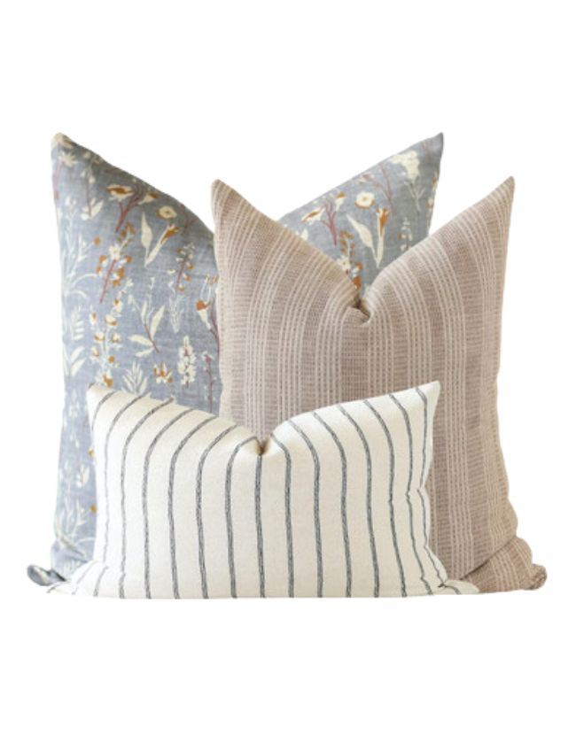 Four decorative throw pillows arranged together create classic cozy living room decor: a blue floral pattern, a beige textured design, and two in front with beige stripes on white and a beige woven look.