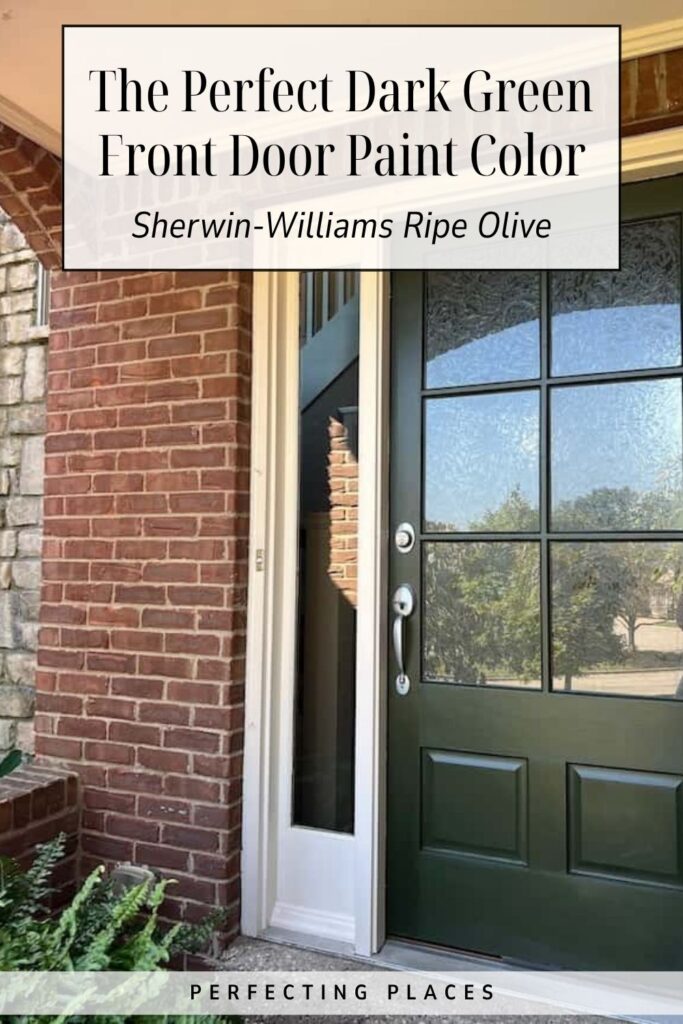 A brick house with a dark green front door, painted in Sherwin-Williams Ripe Olive—an ideal choice if you’re searching for the perfect dark green front door paint color—sits next to a crisp white-framed window.