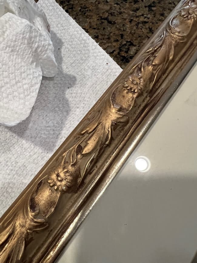 A close-up of an ornate, gold-painted frame with floral designs rests on a countertop next to a textured white paper towel—perfect for displaying your favorite free fine art prints.