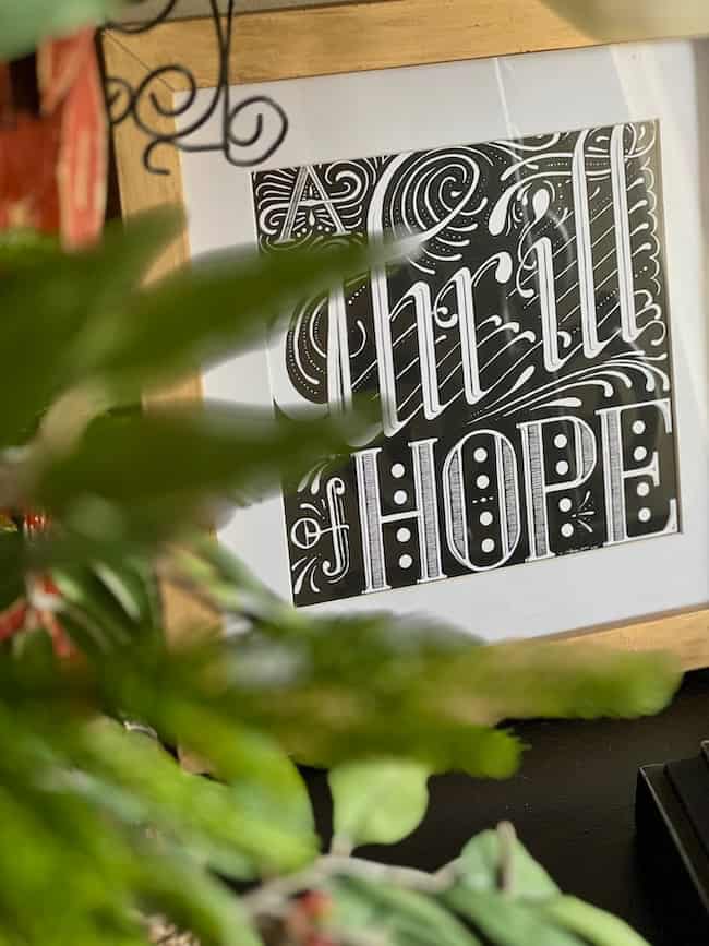 A framed black and white artwork with the words "Thrill of HOPE" in decorative lettering, partially obscured by green leaves, adds a festive touch perfect for a traditional plaid Christmas home tour.